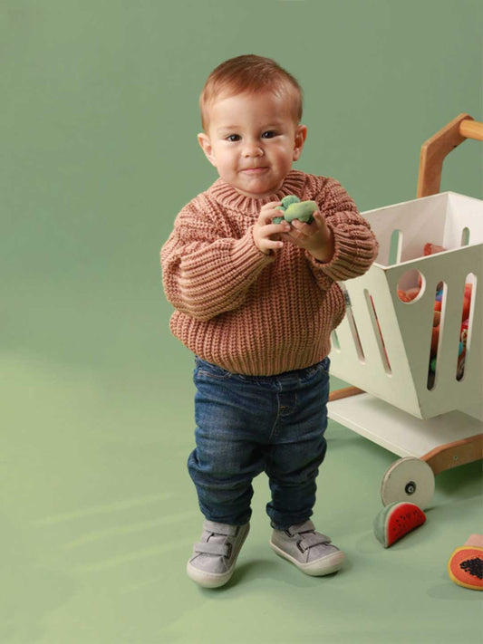 Bebé usando zapatos respetuosos para bebé gris con diseño de animales, mientras da sus primeros pasos con total comodidad y seguridad.