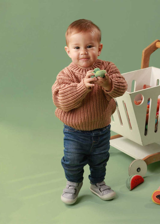 Bebé usando zapatos respetuosos para bebé gris con diseño de animales, mientras da sus primeros pasos con total comodidad y seguridad.