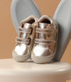 Zapatos respetuosos dorados para bebé pre-caminadores con cierre de velcro, diseño ergonómico y zona delantera espaciosa, ideales para los primeros pasos.