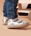 Bebé usando zapatos plateados mientras da sus primeros pasos, con ajuste seguro y flexibilidad para un movimiento natural.